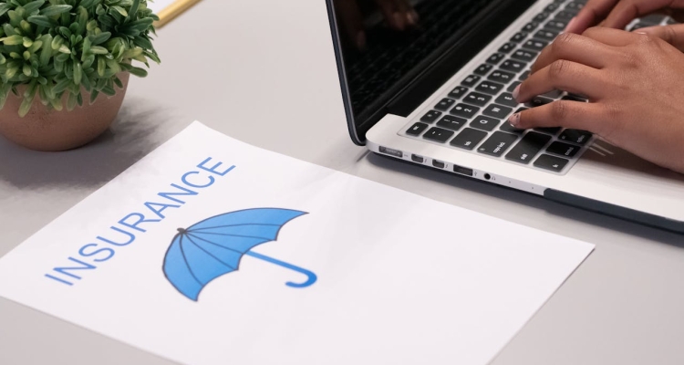 A person typing on a laptop next to a paper that says insurance above an umbrella.