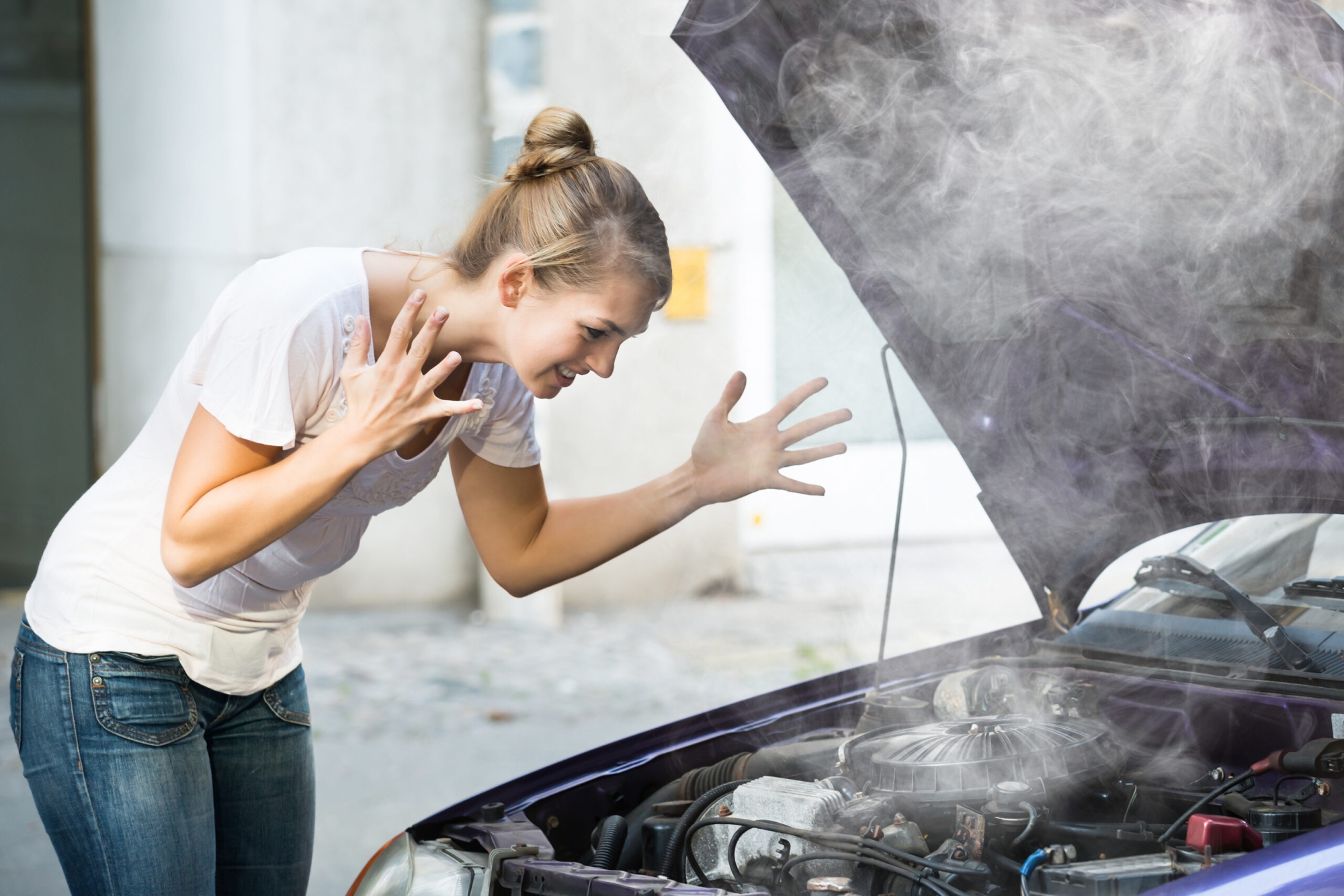 The car overheated and a woman in a white shirt stood next to the smoking engine.