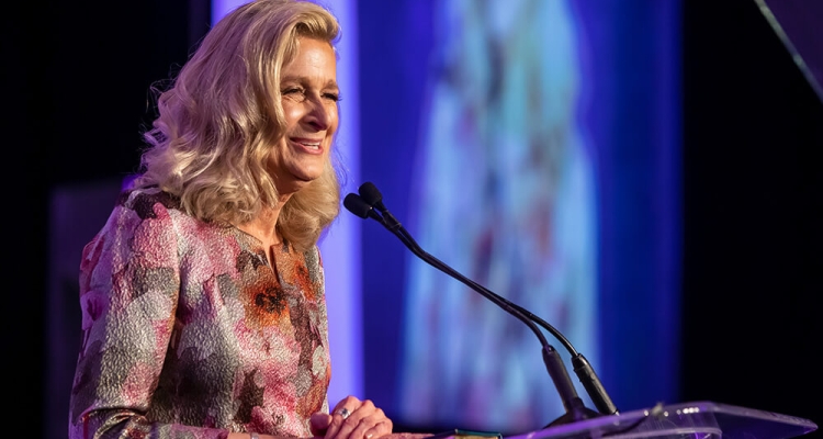 blonde woman speaking at lectern on stage