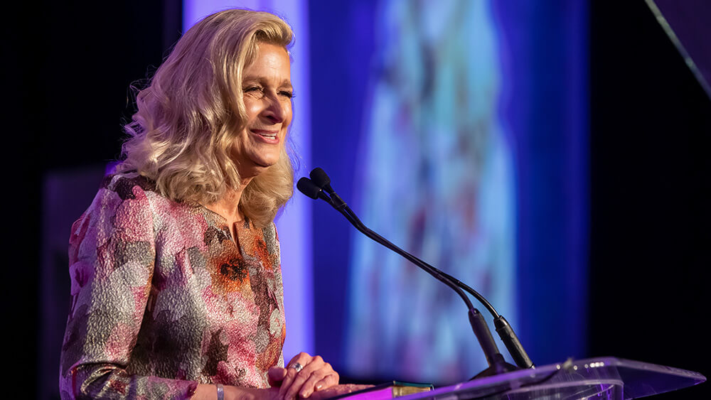 blonde woman speaking at lectern on stage