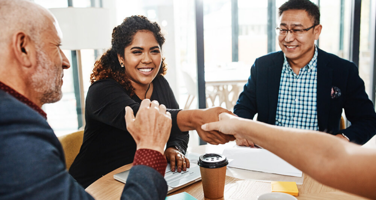 Woman Of Color Shaking Hands With Someone As Two Men Watch At Conference Table