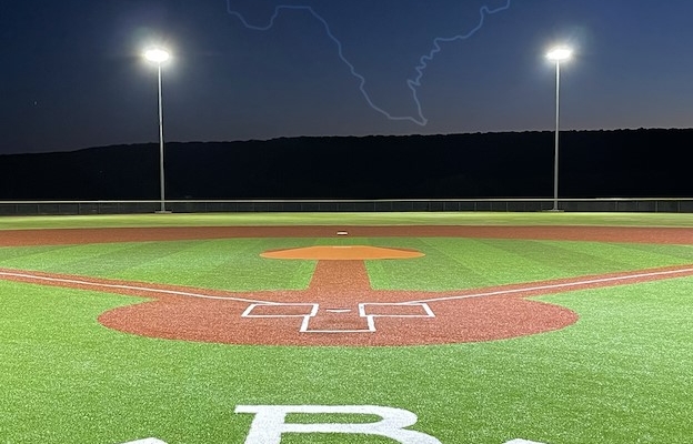 A baseball field with the logos for Unrivaled Sports and Rocker B Ranch above it.